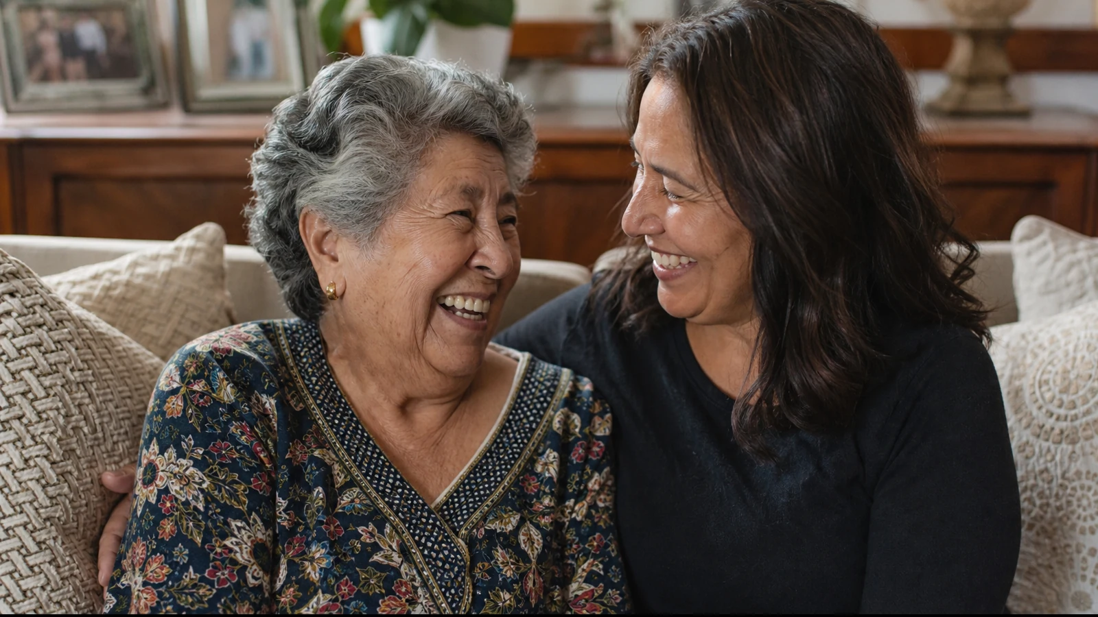 An older mother and her adult daughter laughing together on a couch